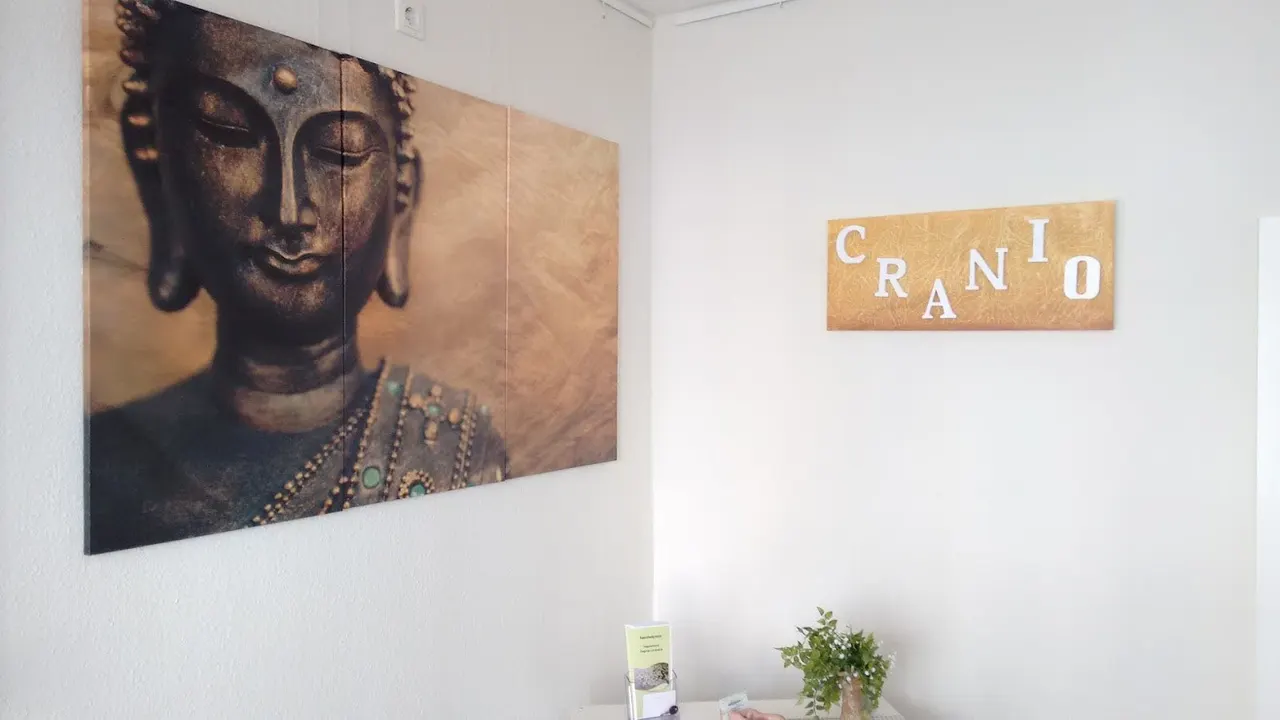 Behandlungsraum mit Buddha-Bild und dem goldenen CRANIO-Schild an der Wand